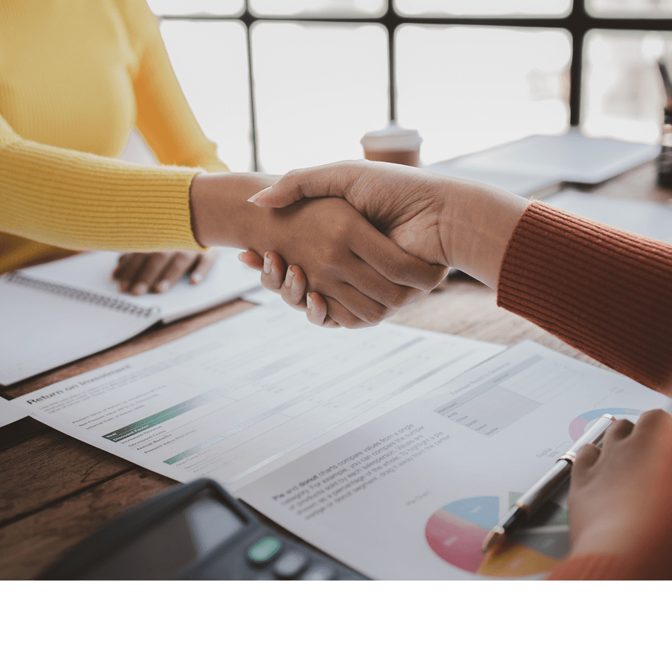 Two people shaking hands over financial documents