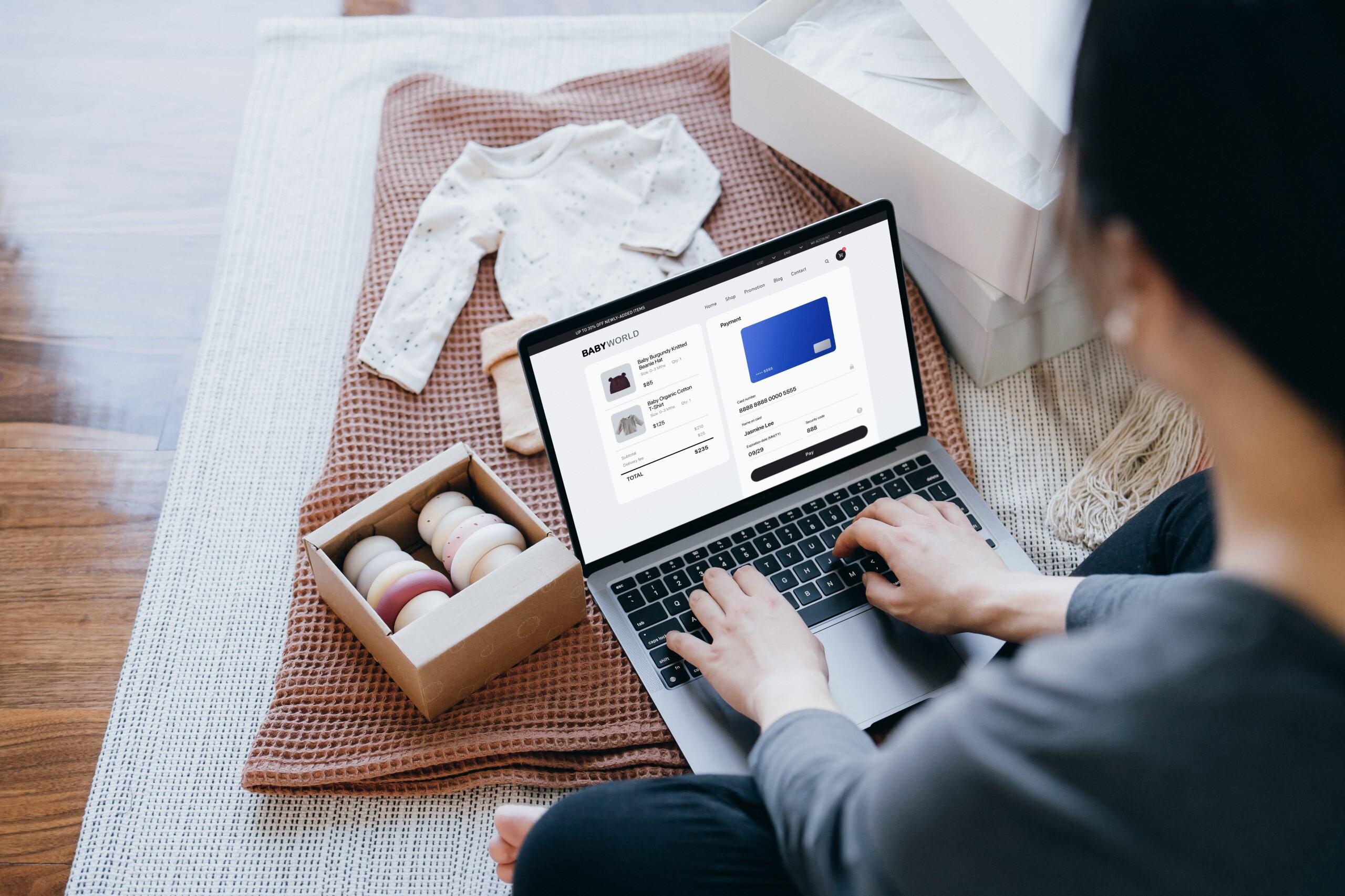 Woman typing on a computer in a store with clothing and products next to her